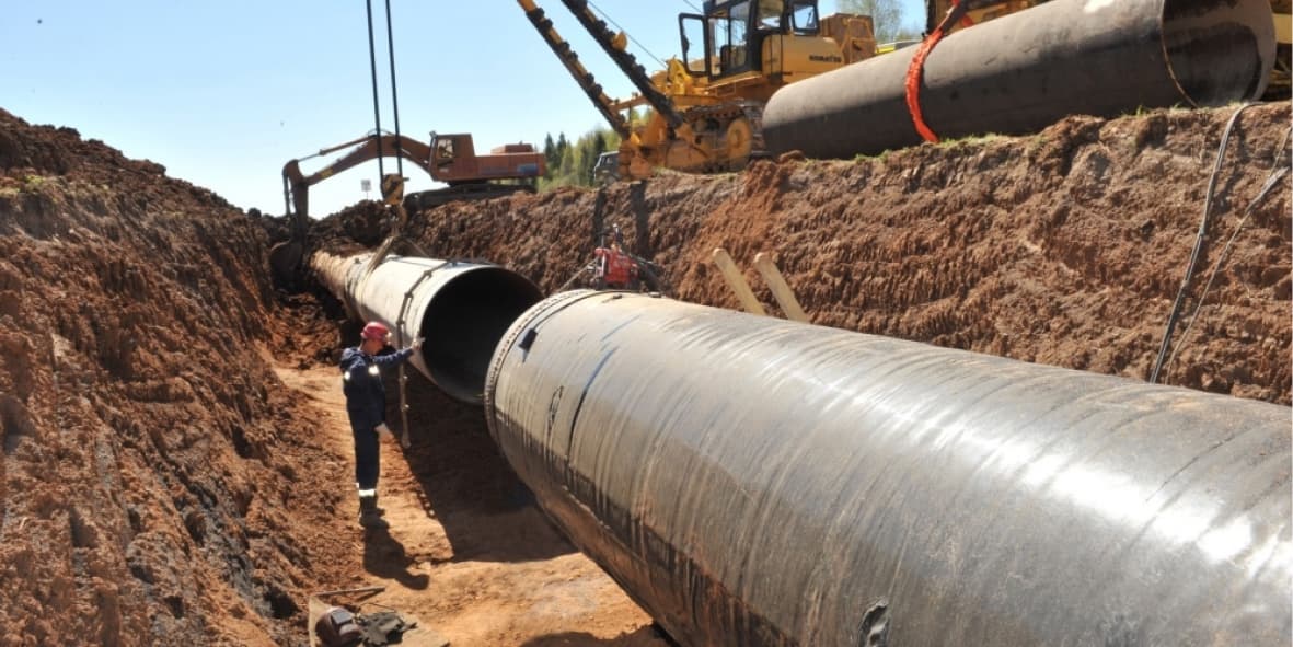 Obra de instalación de tubería de Diámetros Mayores en una zanja, con un trabajador supervisando el proceso y maquinaria en funcionamiento.