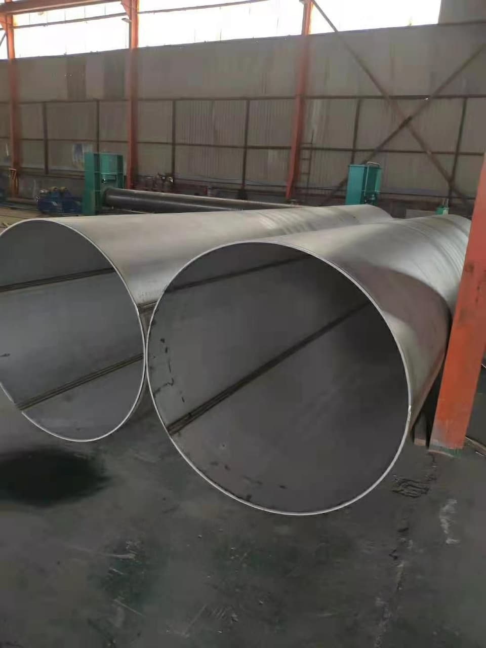 Tubería de Diámetros Mayores de acero, ubicada en un ambiente industrial, con un fondo que muestra maquinaria y estructuras de soporte.