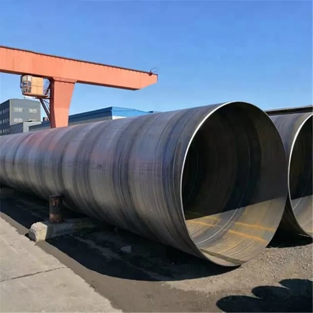Tubería de Diámetros Mayores de acero apilada en un área industrial, con un grúa en el fondo y un cielo despejado.